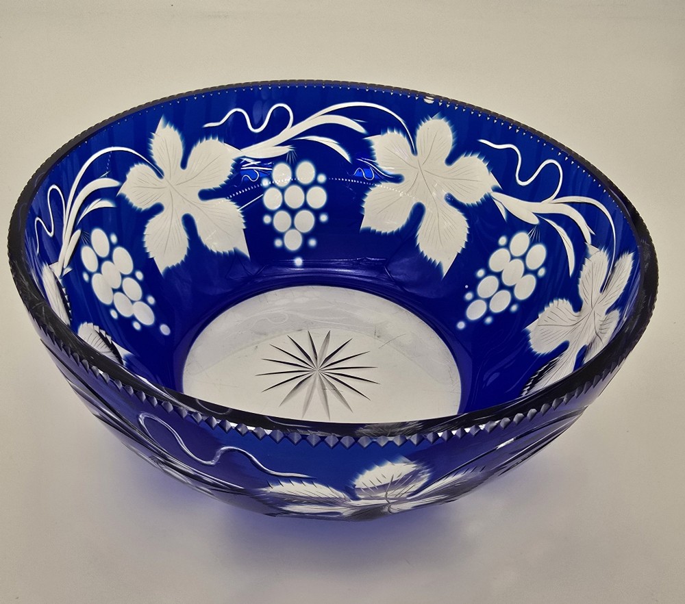 A large round Bohemian cobalt blue cut-to-clear glass bowl featuring etched grapevine leaves, grape clusters, and a serrated rim. View VII