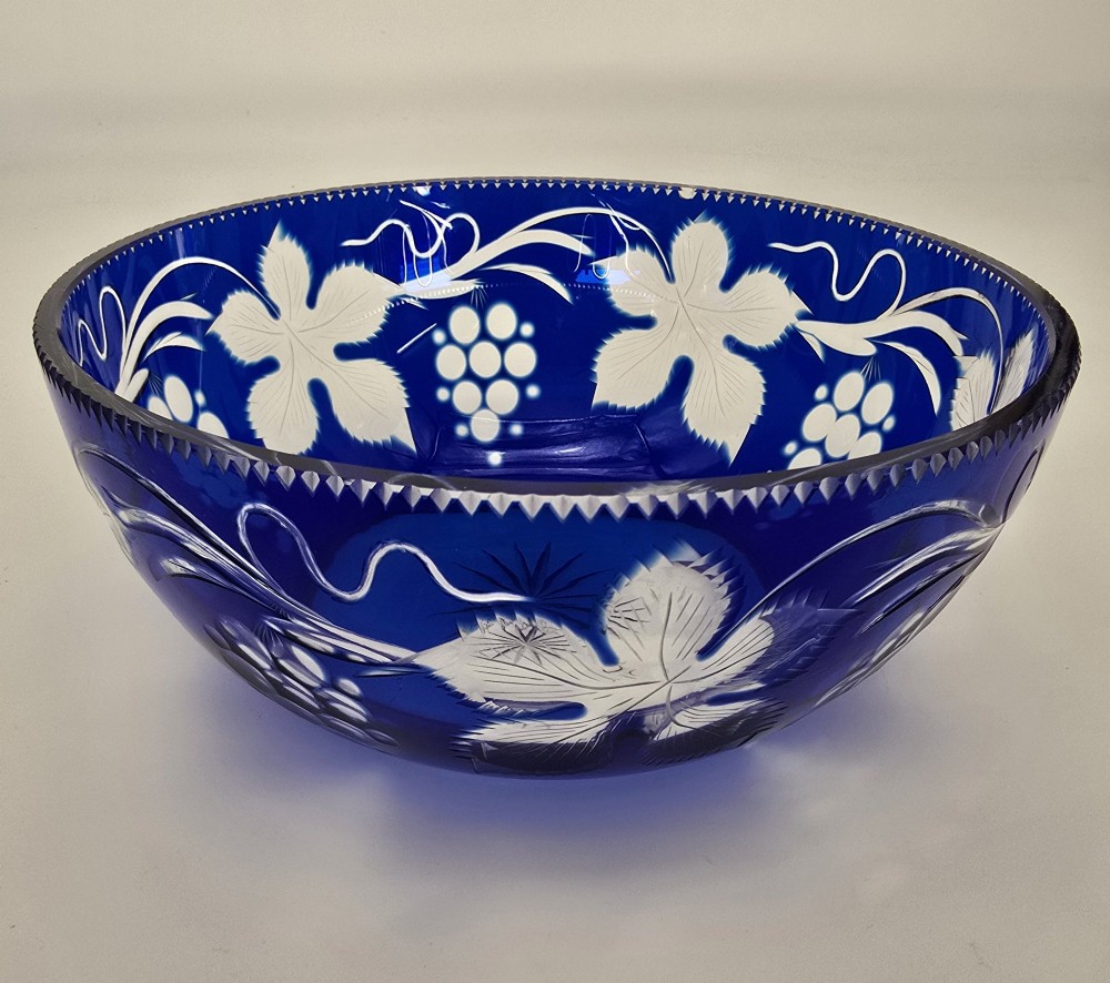 A large round Bohemian cobalt blue cut-to-clear glass bowl featuring etched grapevine leaves, grape clusters, and a serrated rim. View IX