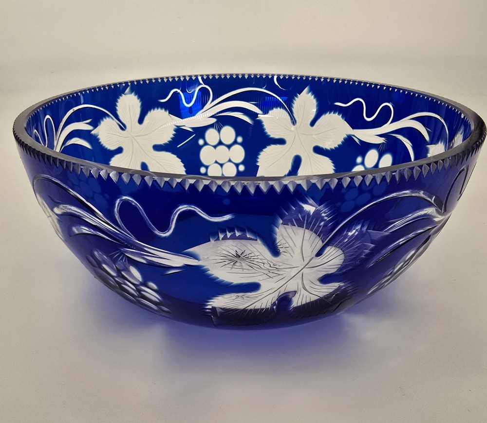 A large round Bohemian cobalt blue cut-to-clear glass bowl featuring etched grapevine leaves, grape clusters, and a serrated rim. View XI