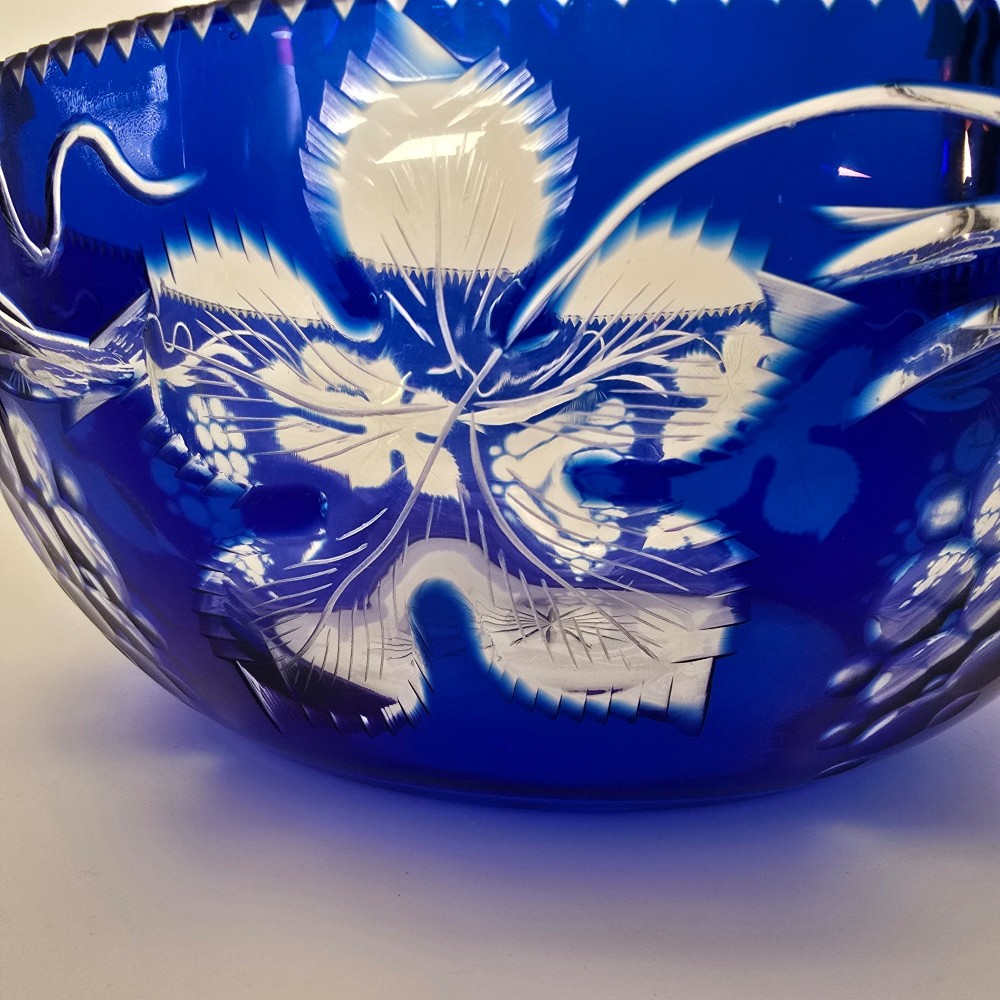 A large round Bohemian cobalt blue cut-to-clear glass bowl featuring etched grapevine leaves, grape clusters, and a serrated rim. View XII