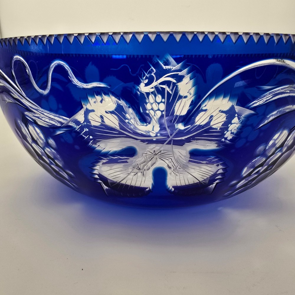 A large round Bohemian cobalt blue cut-to-clear glass bowl featuring etched grapevine leaves, grape clusters, and a serrated rim. View XIII