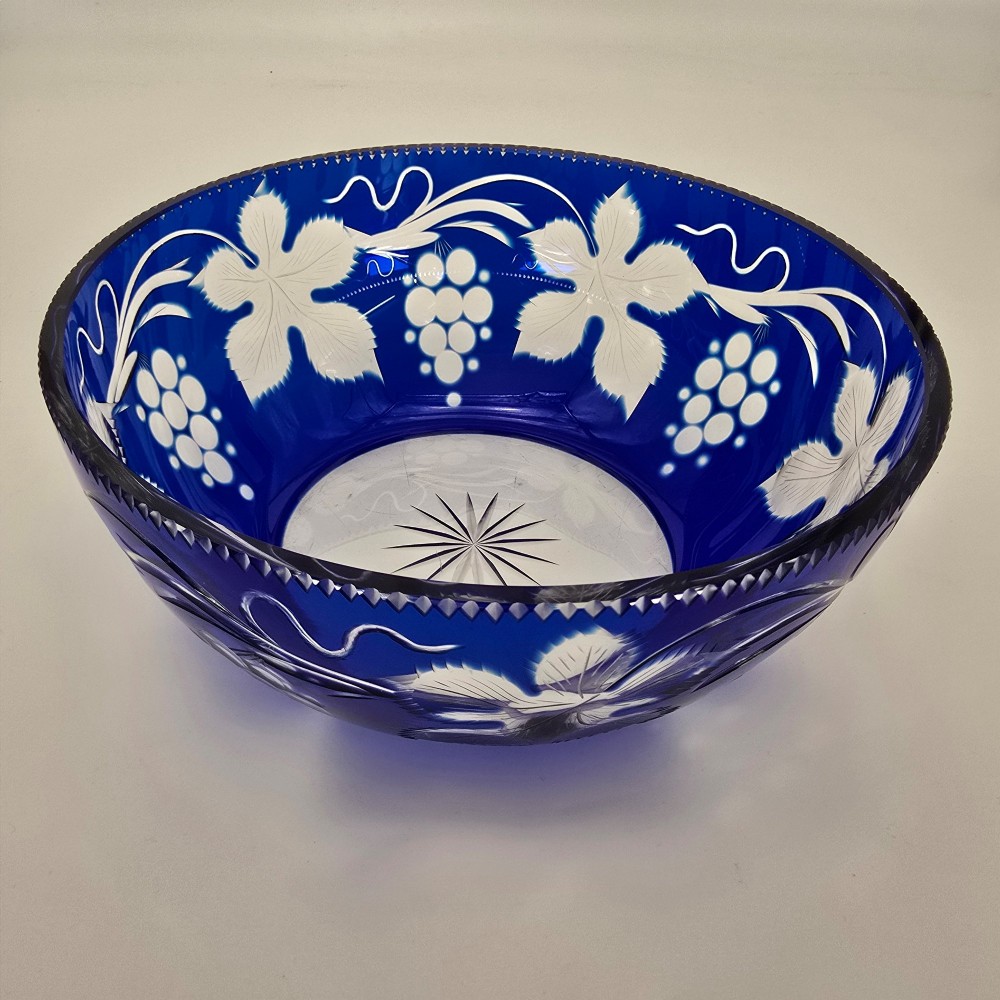 A large round Bohemian cobalt blue cut-to-clear glass bowl featuring etched grapevine leaves, grape clusters, and a serrated rim. View XV