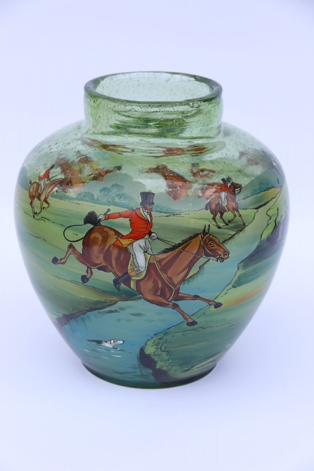 A bulbous green hand-blown glass vase featuring a hand-painted enamel scene of fox hunters riding horses across a landscape.