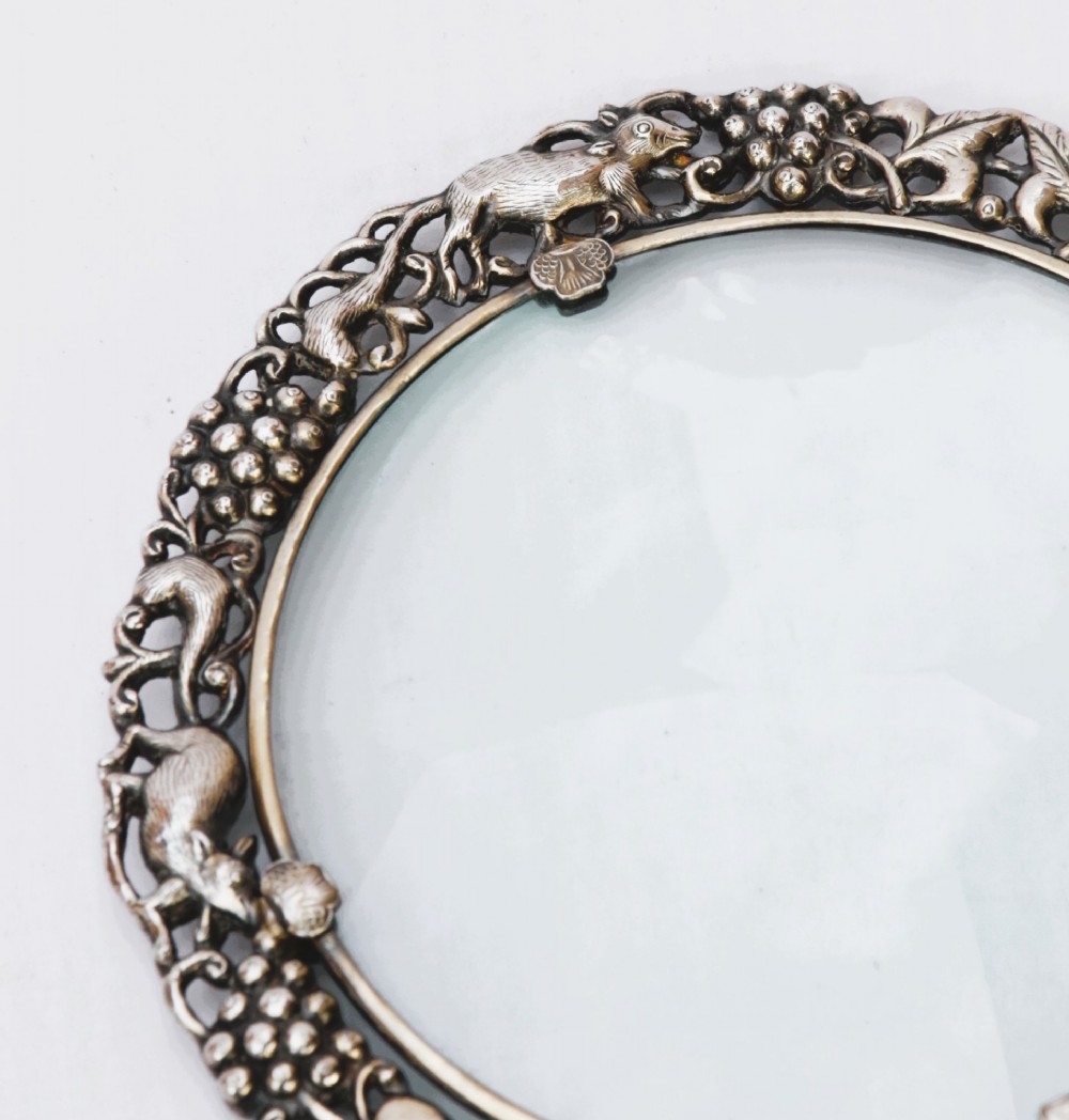 A late 19th-century Chinese silver magnifying glass featuring a carved white jade handle and an openwork grapevine frame with animal details. View X