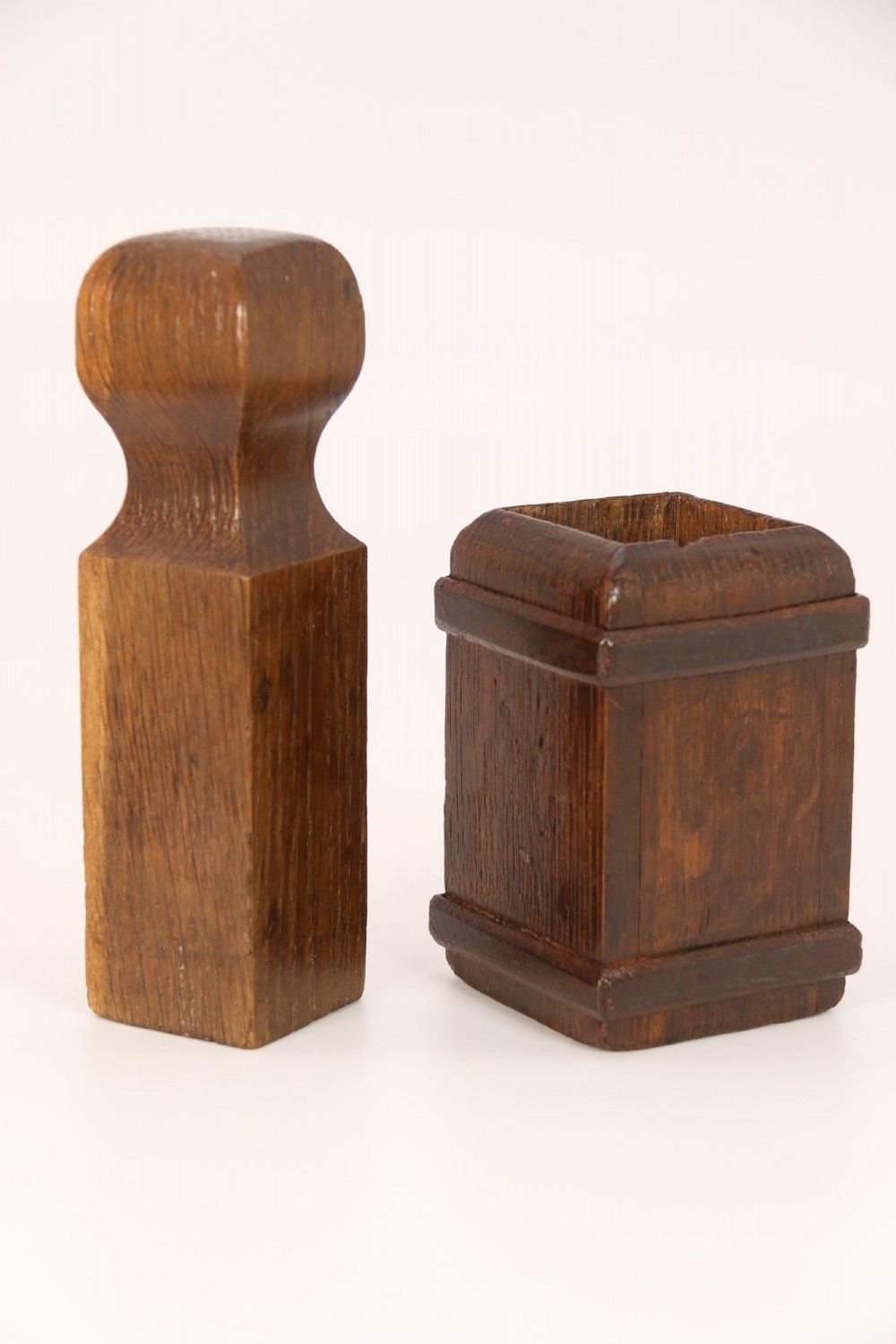 An antique dark oak apothecary crusher set consisting of a square wooden vessel with iron mounts alongside a matching rectangular wooden plunger with a shaped handle. View II