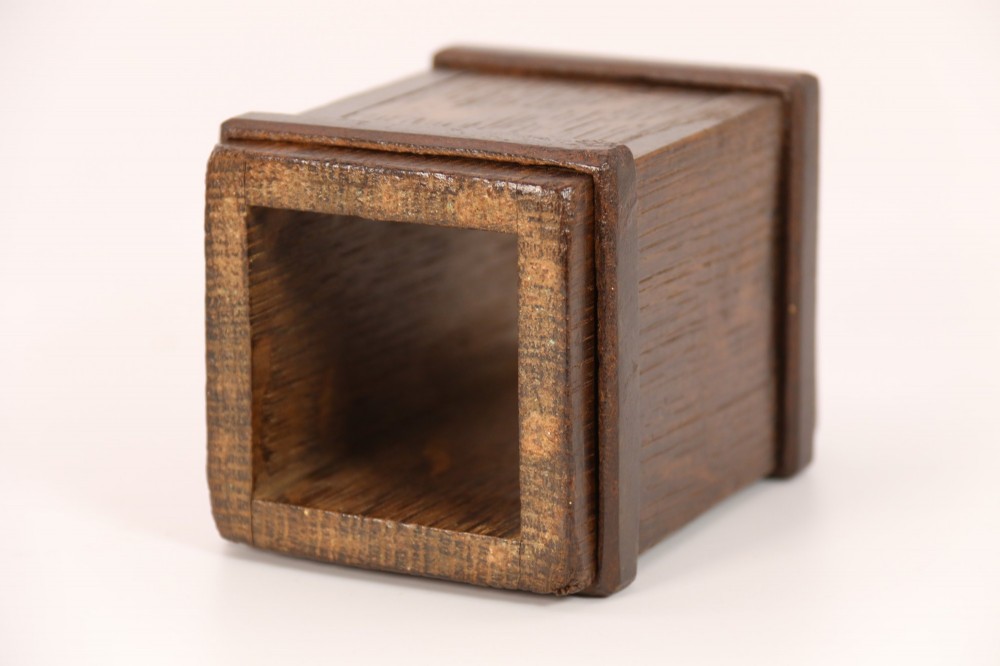 An antique dark oak apothecary crusher set consisting of a square wooden vessel with iron mounts alongside a matching rectangular wooden plunger with a shaped handle. View IX