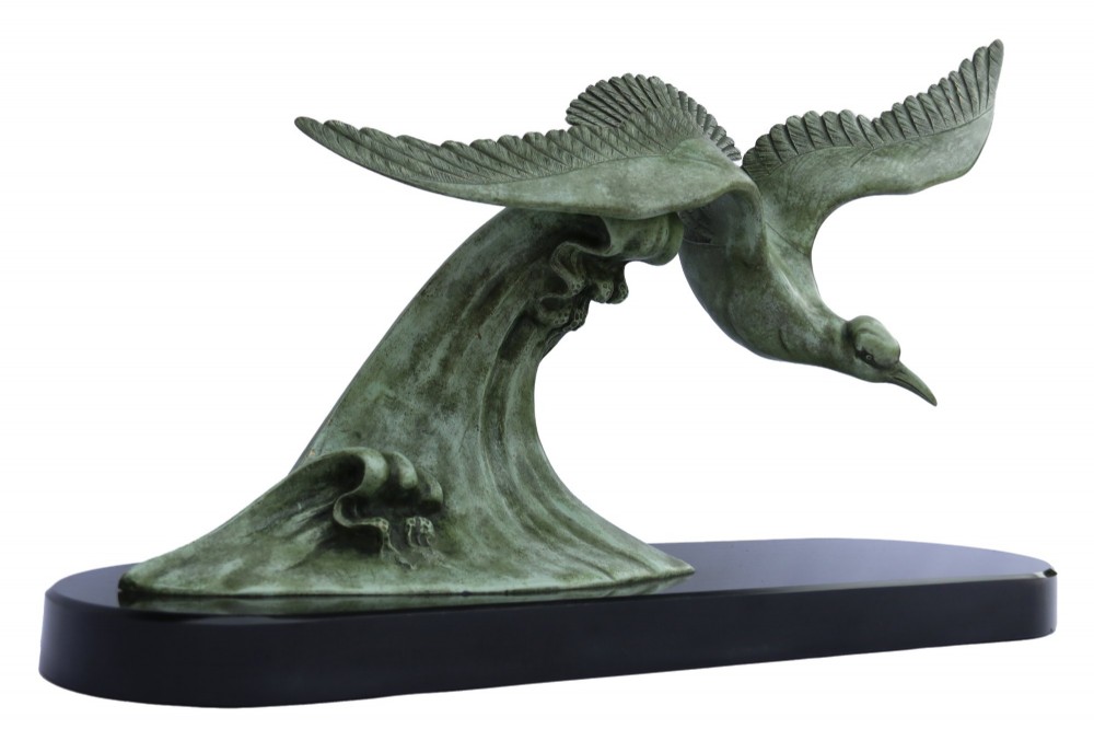 A patinated green bronze sculpture depicting an albatross with extended wings skimming a crested wave, mounted on an oval black marble plinth.