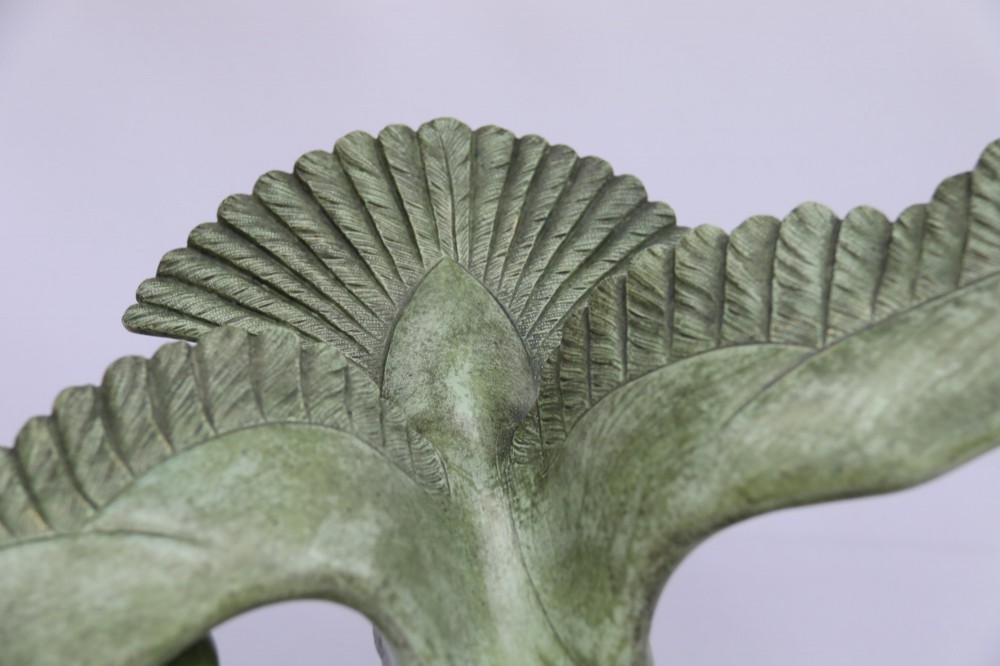 A patinated green bronze sculpture depicting an albatross with extended wings skimming a crested wave, mounted on an oval black marble plinth. View V