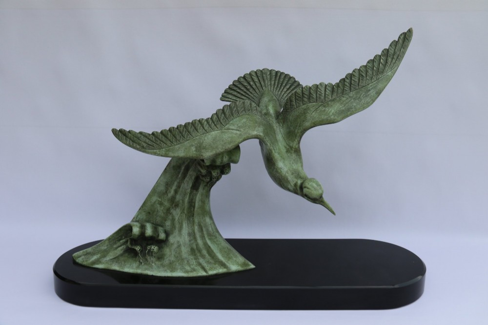 A patinated green bronze sculpture depicting an albatross with extended wings skimming a crested wave, mounted on an oval black marble plinth. View IX