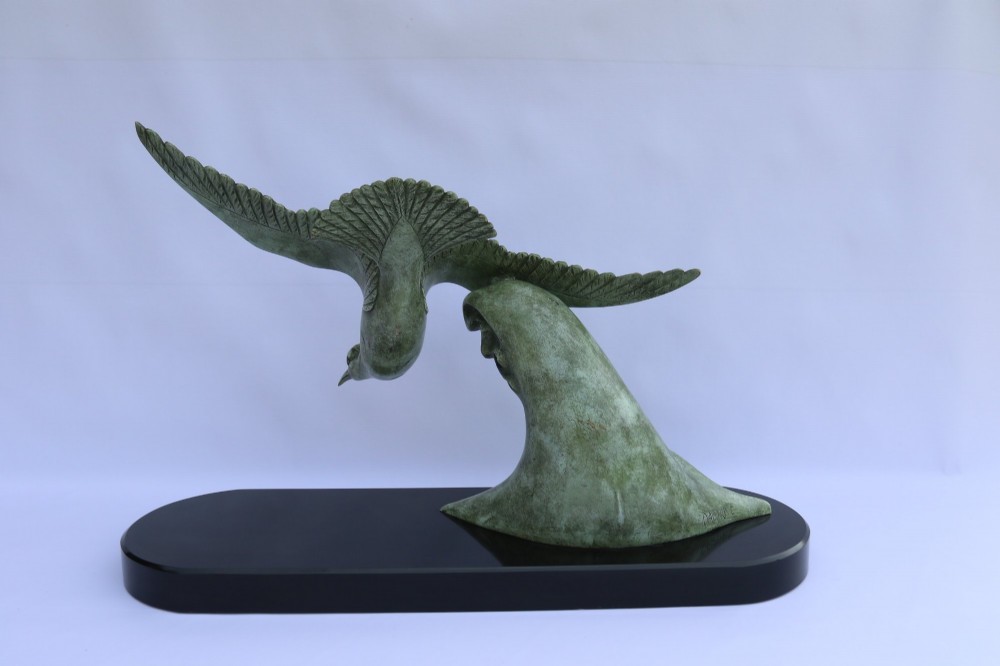 A patinated green bronze sculpture depicting an albatross with extended wings skimming a crested wave, mounted on an oval black marble plinth. View X