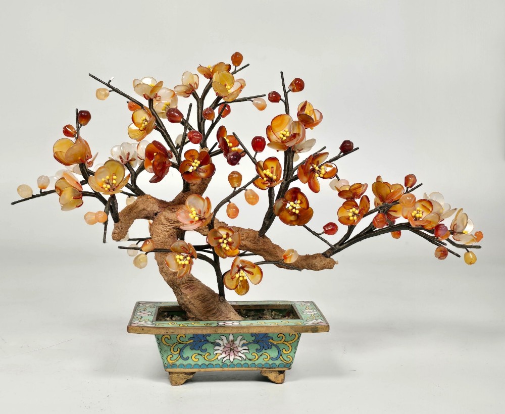A Chinese decorative bonsai tree featuring carved amber-coloured hardstone plum blossoms on wired branches set inside a turquoise floral cloisonne planter.