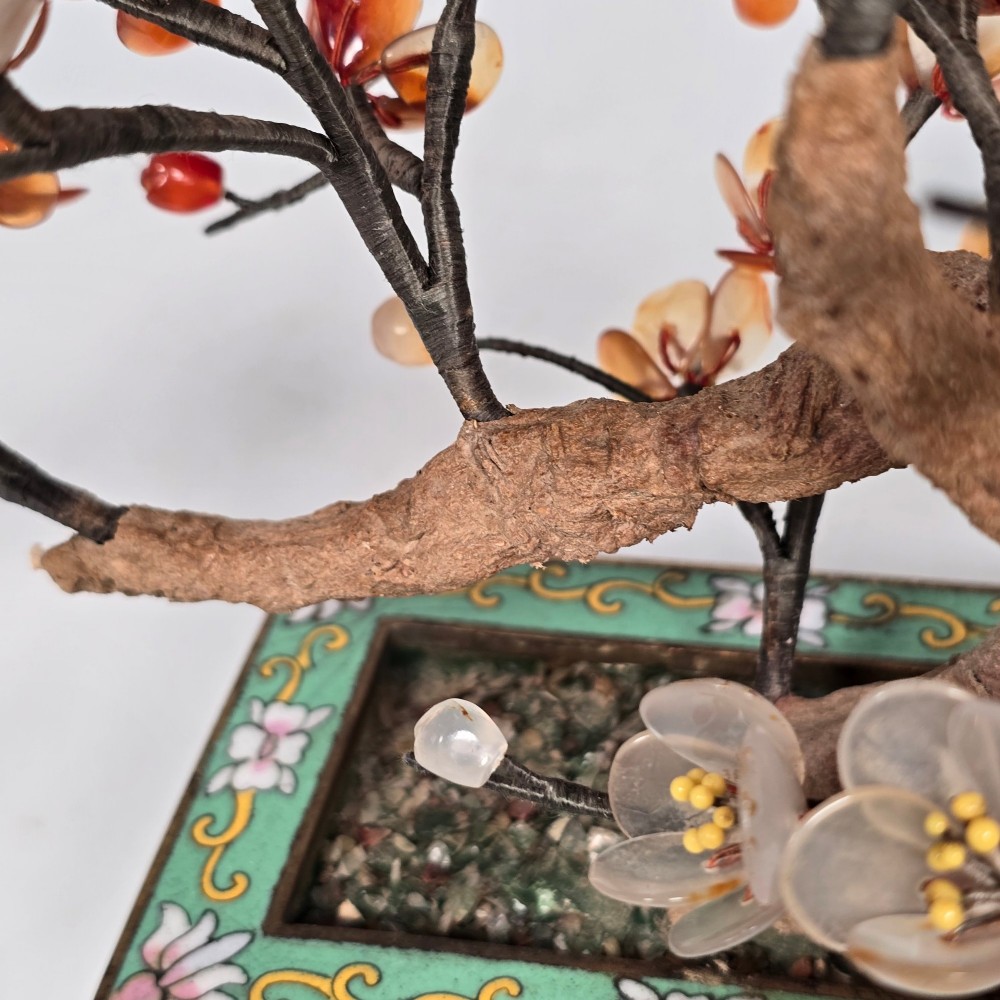A Chinese decorative bonsai tree featuring carved amber-coloured hardstone plum blossoms on wired branches set inside a turquoise floral cloisonne planter. View X