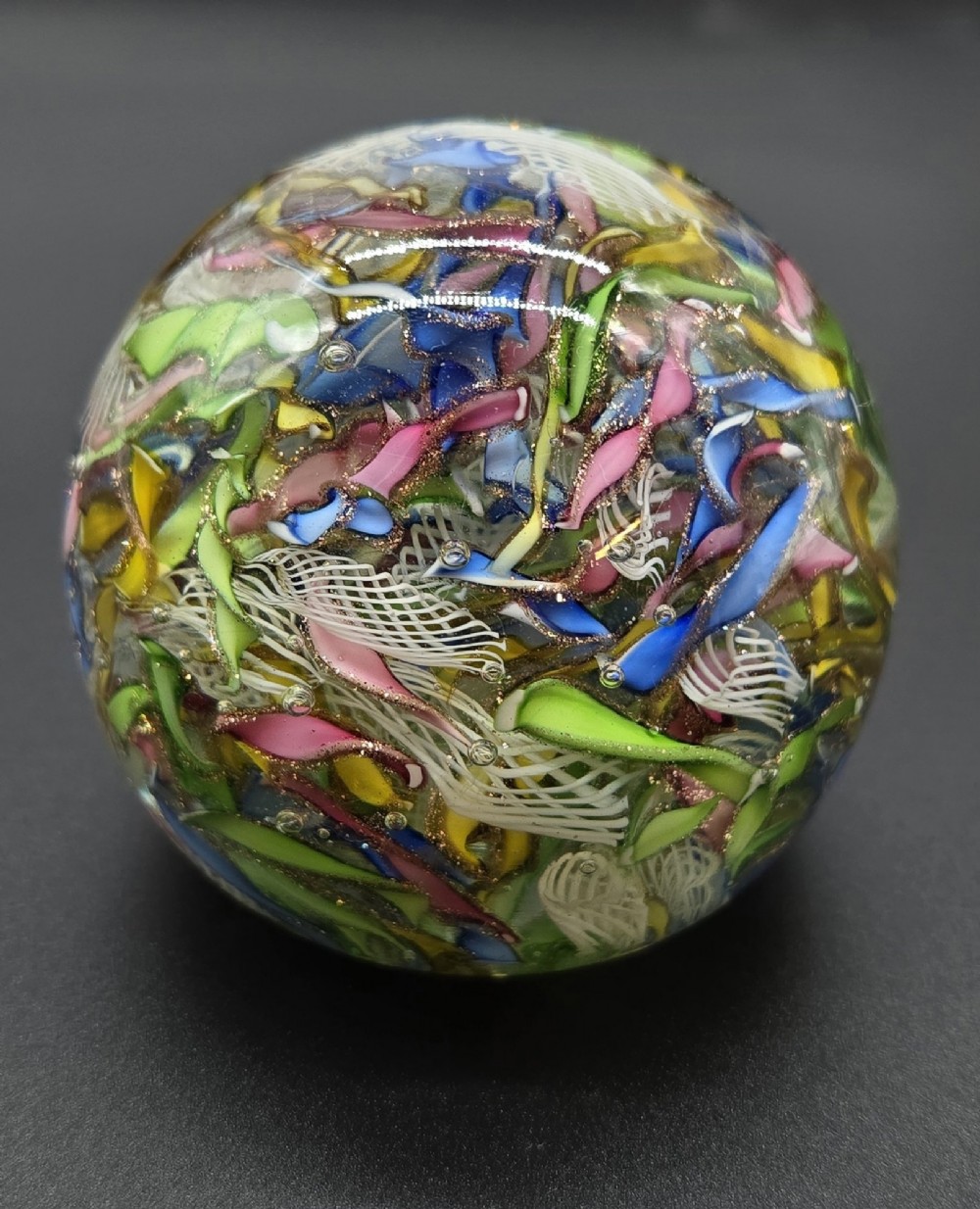A clear spherical glass paperweight filled with an intricate mix of colourful cane fragments, white filigree ribbons, and glittering gold aventurine flecks.