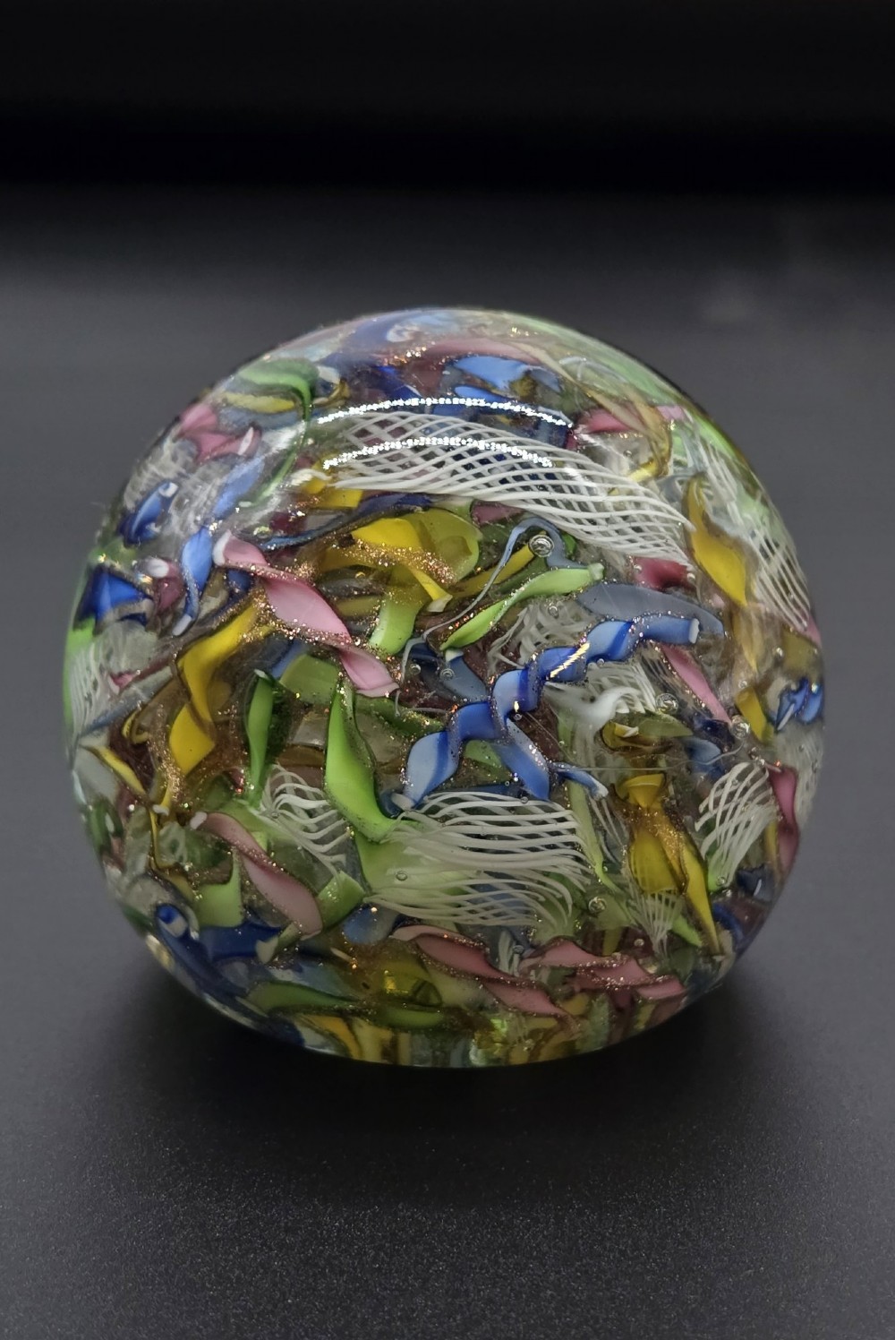 A clear spherical glass paperweight filled with an intricate mix of colourful cane fragments, white filigree ribbons, and glittering gold aventurine flecks. View III