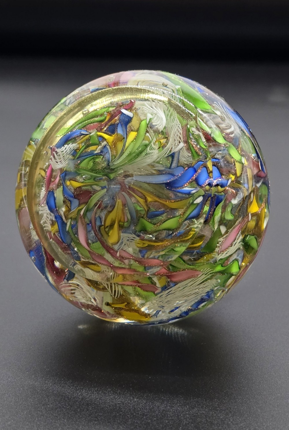 A clear spherical glass paperweight filled with an intricate mix of colourful cane fragments, white filigree ribbons, and glittering gold aventurine flecks. View IV