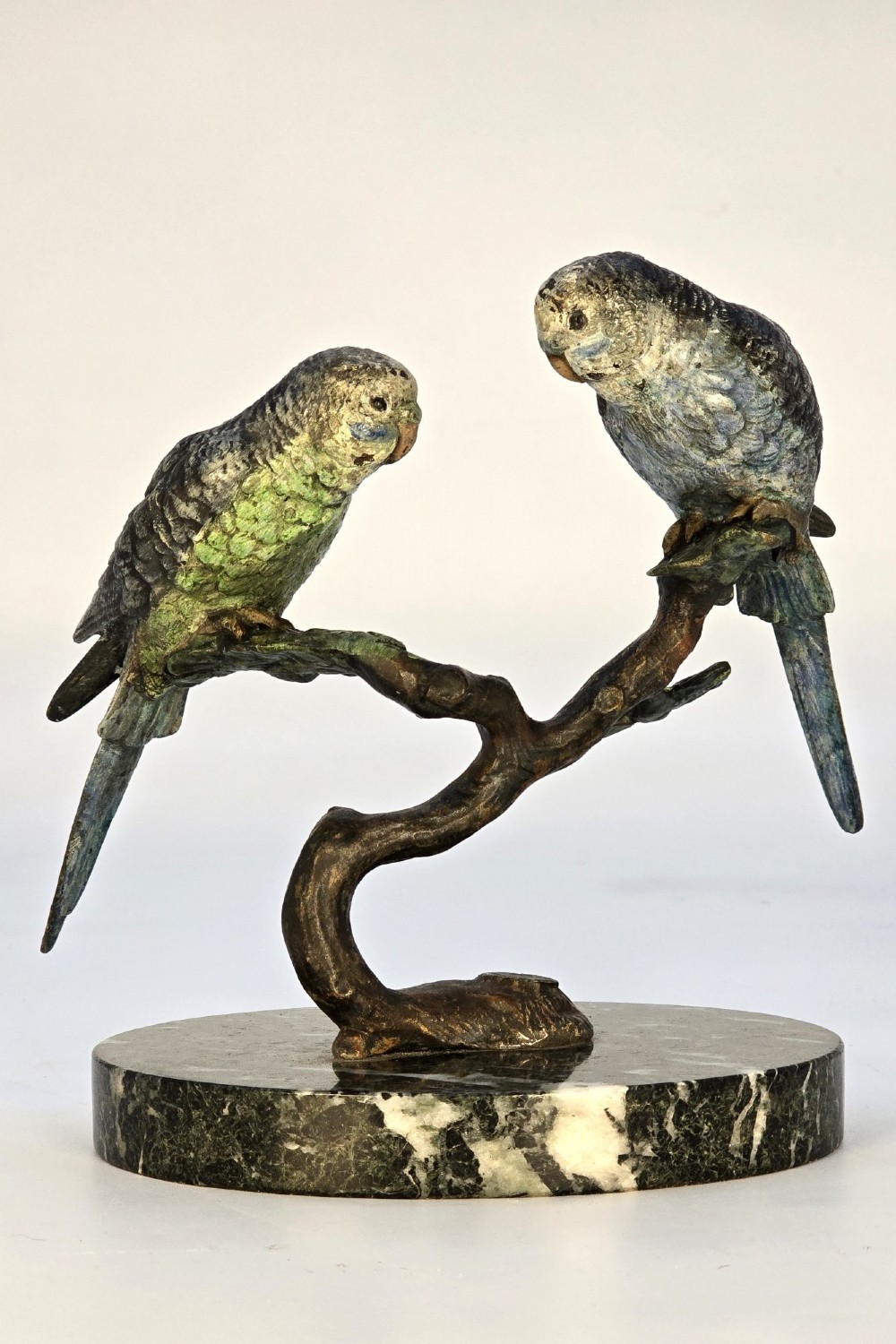 A cold-painted bronze sculpture featuring two budgerigars perched on a branch mounted upon a round green marble base.