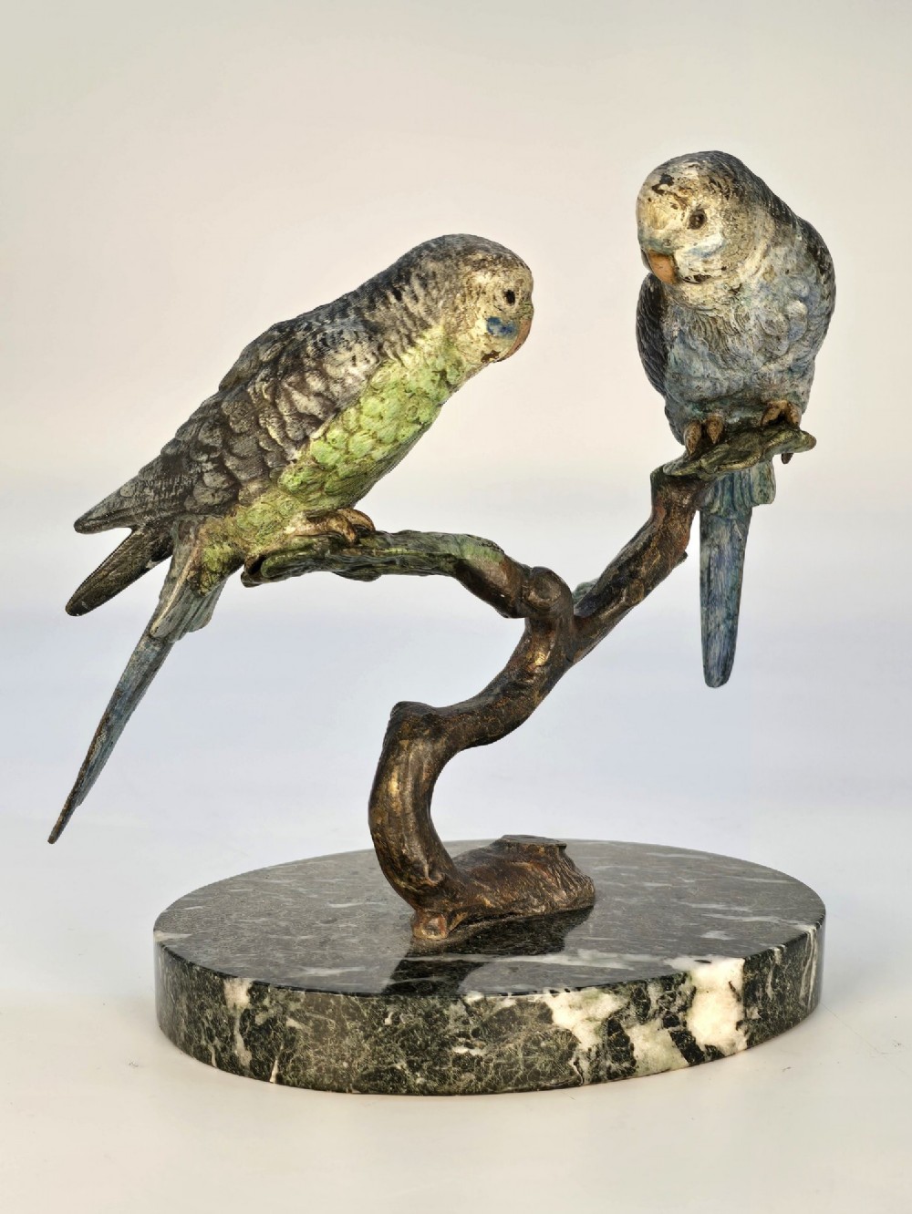 A cold-painted bronze sculpture featuring two budgerigars perched on a branch mounted upon a round green marble base. View X
