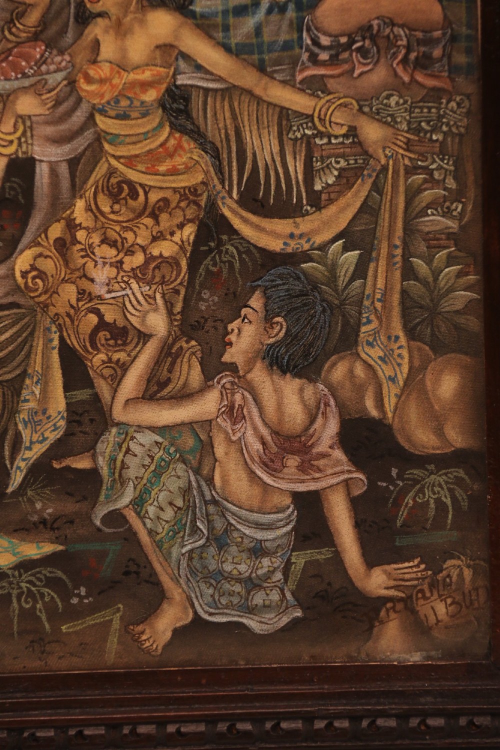 A detailed Balinese painting depicting figures dancing and playing gamelan instruments within a lush landscape, set inside a carved dark wood frame. View IV