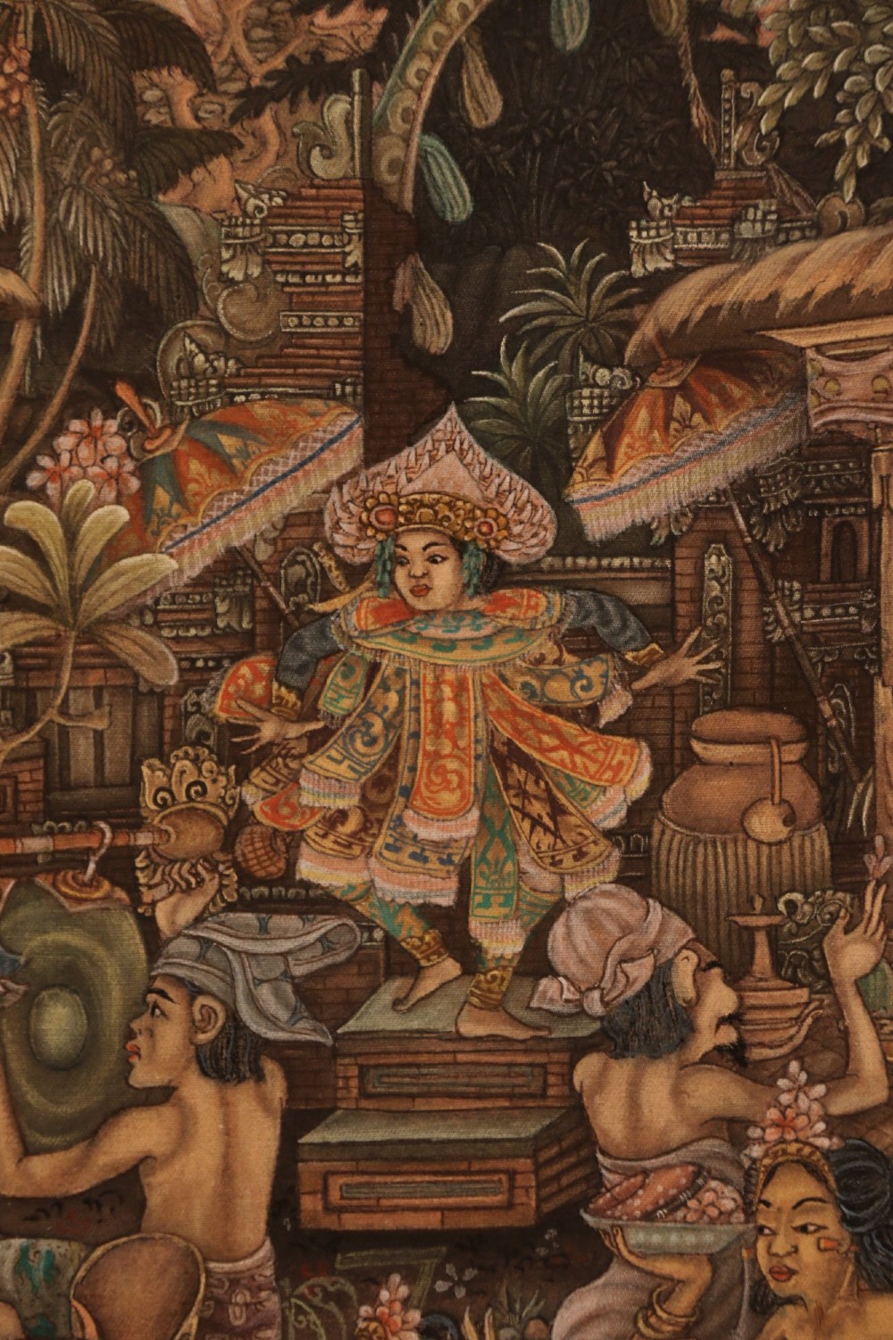 A detailed Balinese painting depicting figures dancing and playing gamelan instruments within a lush landscape, set inside a carved dark wood frame. View VII