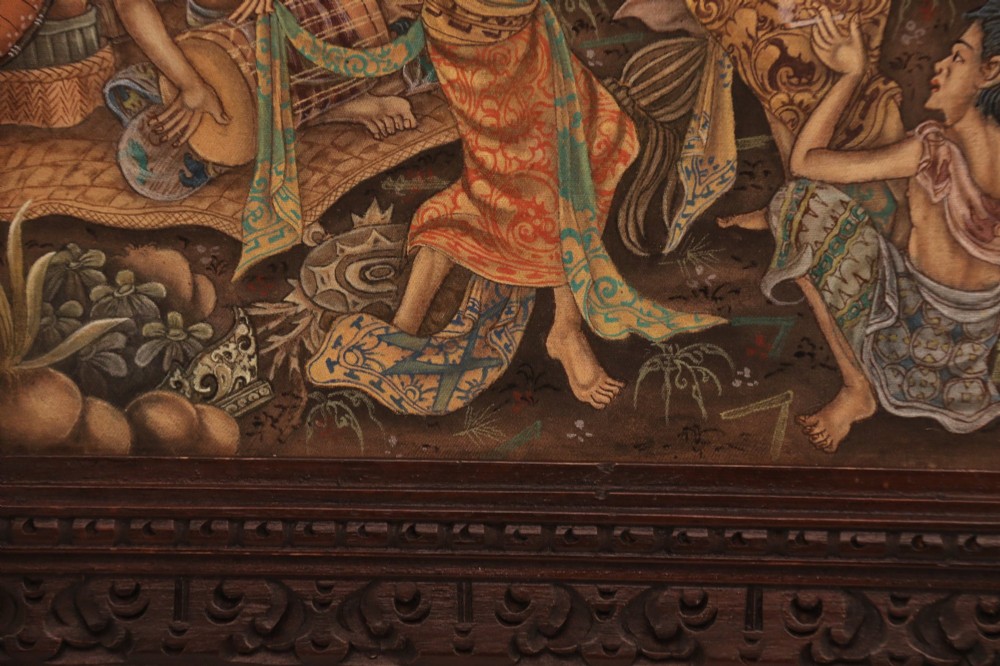 A detailed Balinese painting depicting figures dancing and playing gamelan instruments within a lush landscape, set inside a carved dark wood frame. View IX