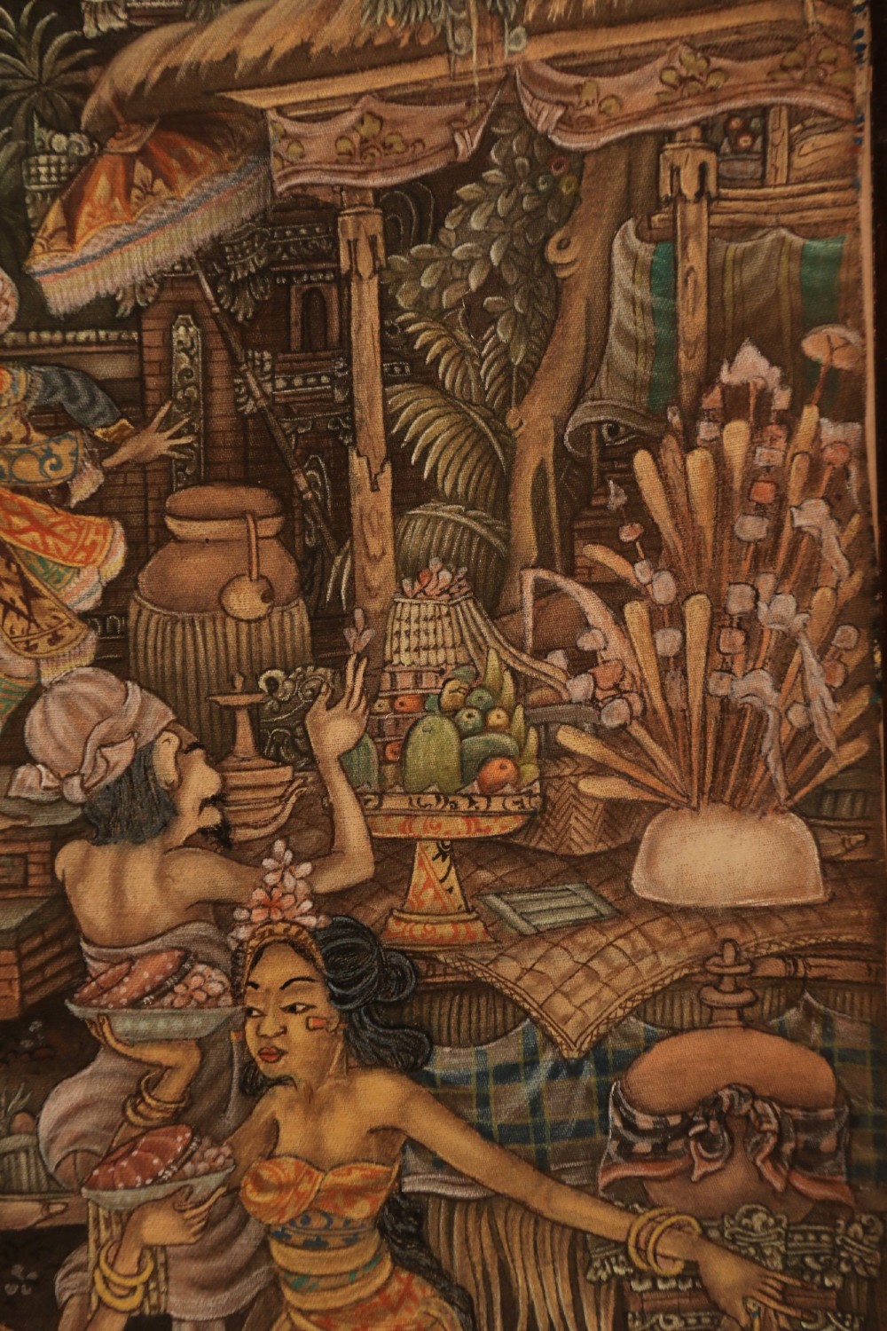 A detailed Balinese painting depicting figures dancing and playing gamelan instruments within a lush landscape, set inside a carved dark wood frame. View XI