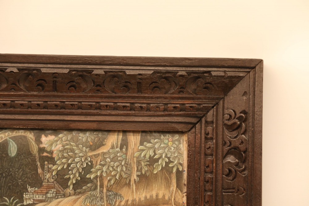 A detailed Balinese painting depicting figures dancing and playing gamelan instruments within a lush landscape, set inside a carved dark wood frame. View XIV