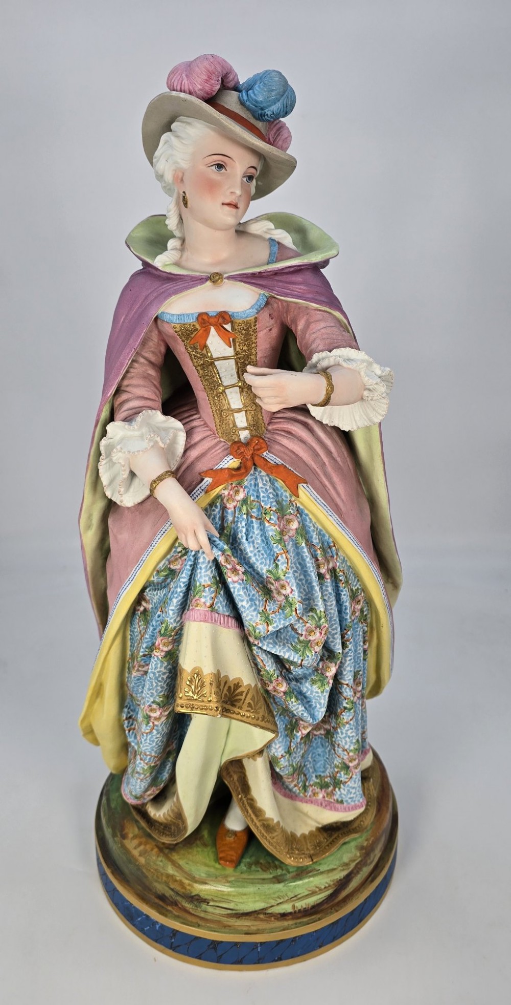 A pair of large hand-painted French porcelain statuettes depicting an 18th-century man and woman in elaborate court attire standing on decorated round pedestals. View V