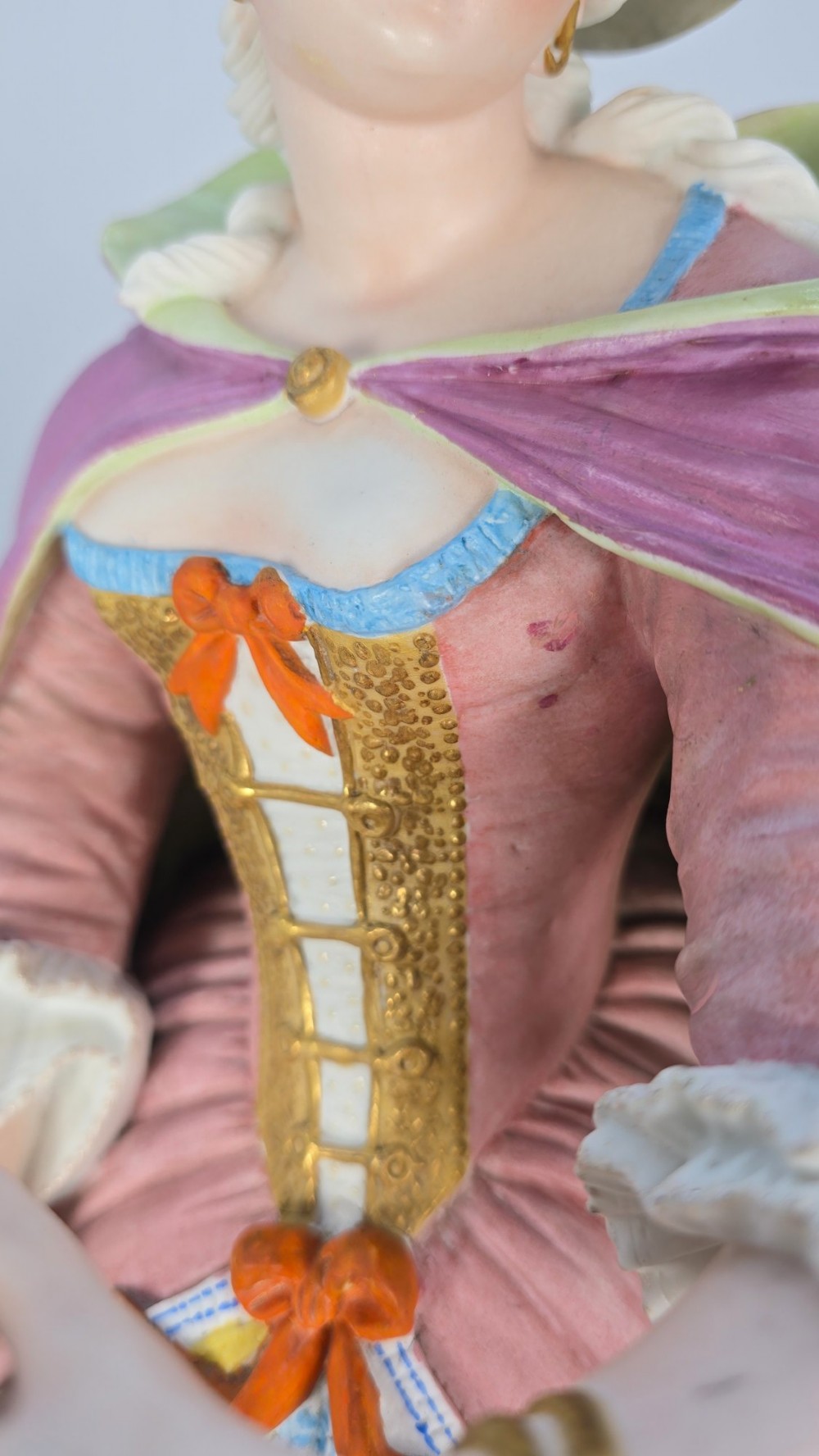 A pair of large hand-painted French porcelain statuettes depicting an 18th-century man and woman in elaborate court attire standing on decorated round pedestals. View IX