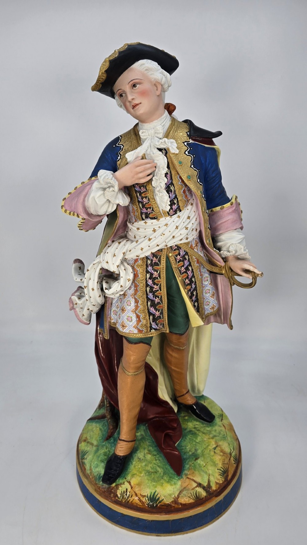 A pair of large hand-painted French porcelain statuettes depicting an 18th-century man and woman in elaborate court attire standing on decorated round pedestals. View X