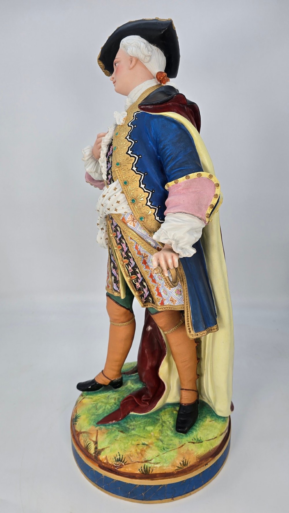 A pair of large hand-painted French porcelain statuettes depicting an 18th-century man and woman in elaborate court attire standing on decorated round pedestals. View XI