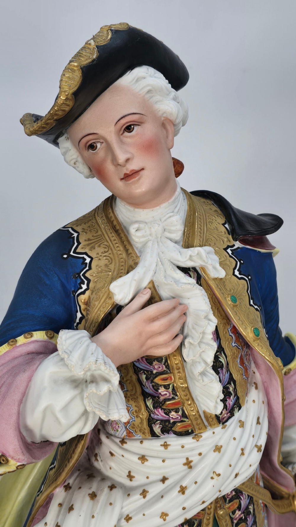 A pair of large hand-painted French porcelain statuettes depicting an 18th-century man and woman in elaborate court attire standing on decorated round pedestals. View XIII