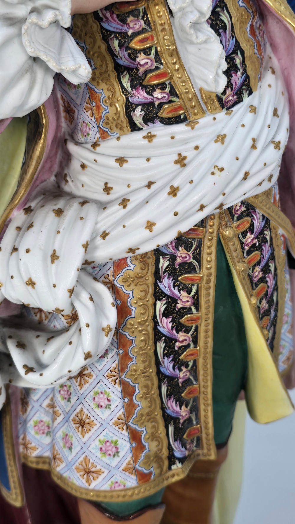 A pair of large hand-painted French porcelain statuettes depicting an 18th-century man and woman in elaborate court attire standing on decorated round pedestals. View XIV