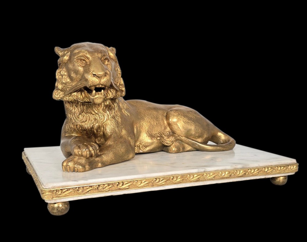 A French gilt bronze figure of a recumbent lion mounted on a rectangular white marble plinth with gilt borders and ball feet.