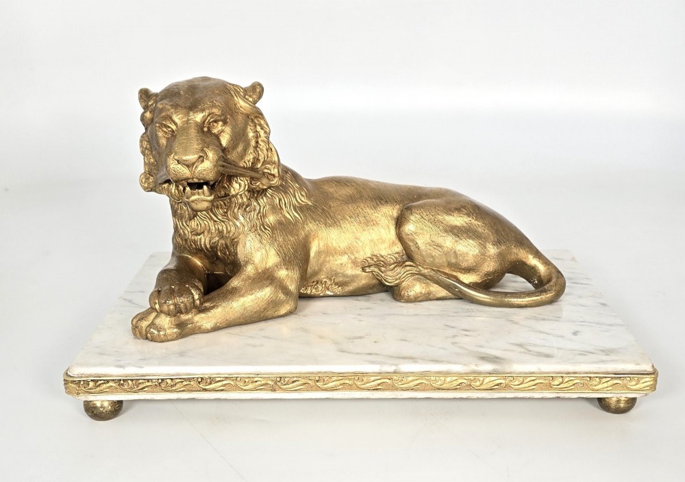 A French gilt bronze figure of a recumbent lion mounted on a rectangular white marble plinth with gilt borders and ball feet. View II