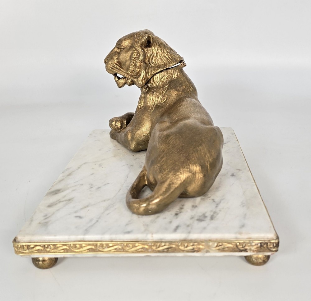 A French gilt bronze figure of a recumbent lion mounted on a rectangular white marble plinth with gilt borders and ball feet. View V