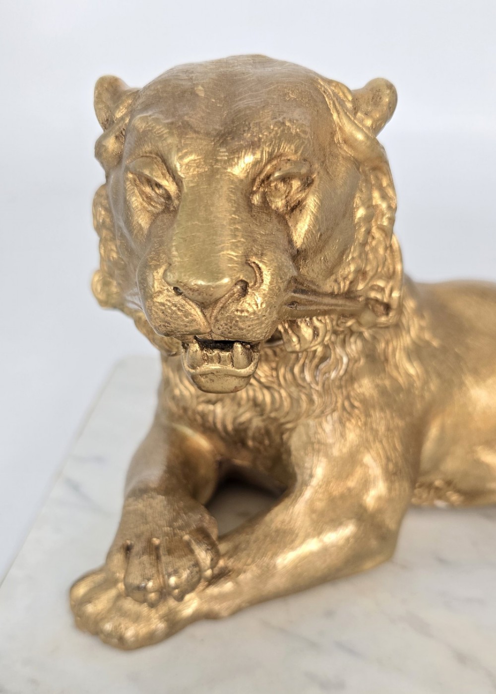 A French gilt bronze figure of a recumbent lion mounted on a rectangular white marble plinth with gilt borders and ball feet. View X