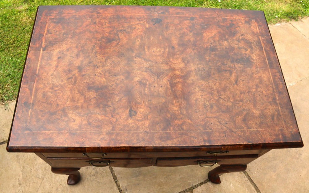 A George II burr elm lowboy featuring three drawers, brass drop handles, a scalloped apron, and cabriole legs terminating in pad feet. View V