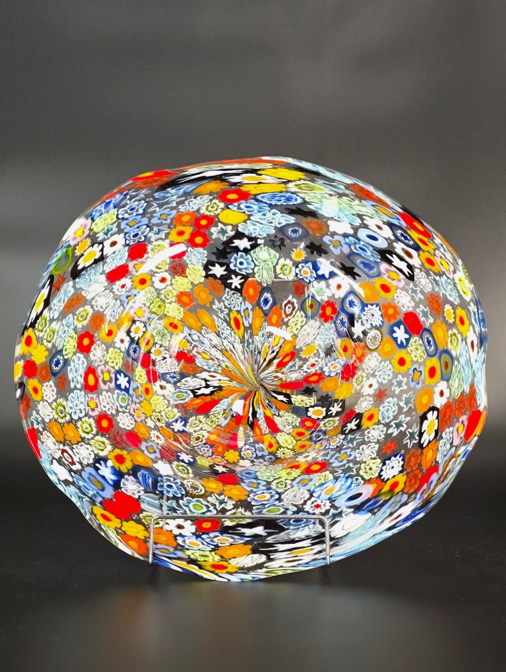 A circular Murano millefiori glass bowl featuring dense, colourful mosaic cane patterns arranged in starburst and floral formations.