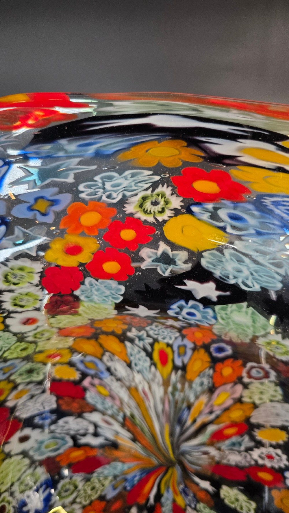 A circular Murano millefiori glass bowl featuring dense, colourful mosaic cane patterns arranged in starburst and floral formations. View V
