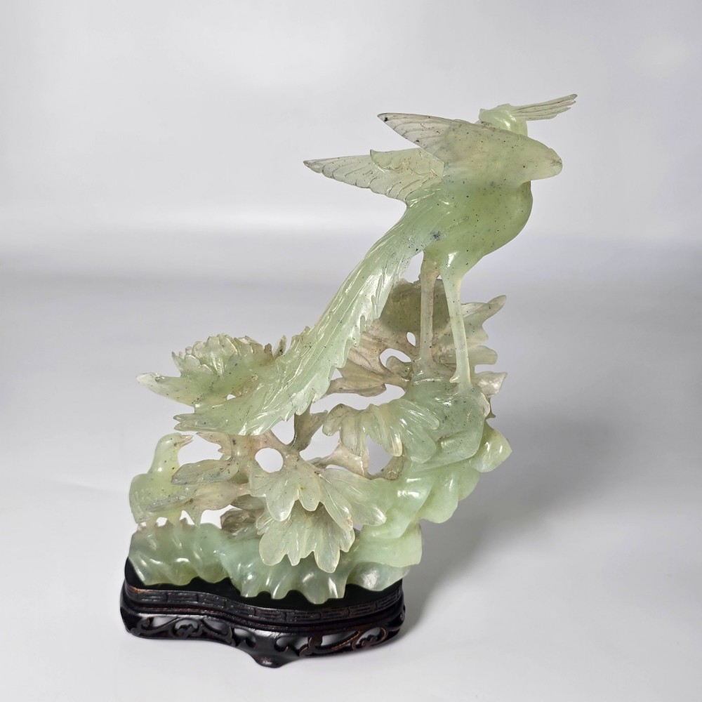 A pale green carved stone sculpture depicting two birds among floral blooms set on a dark carved wood base. View IV