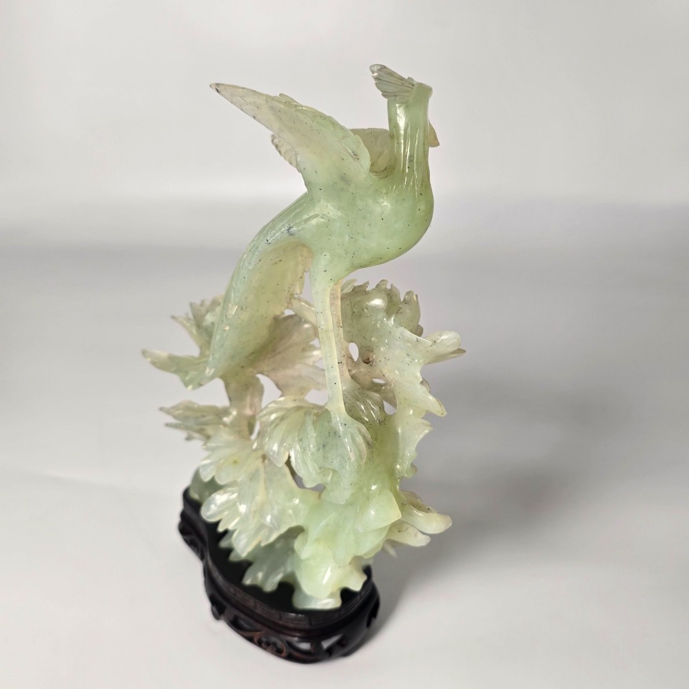 A pale green carved stone sculpture depicting two birds among floral blooms set on a dark carved wood base. View V