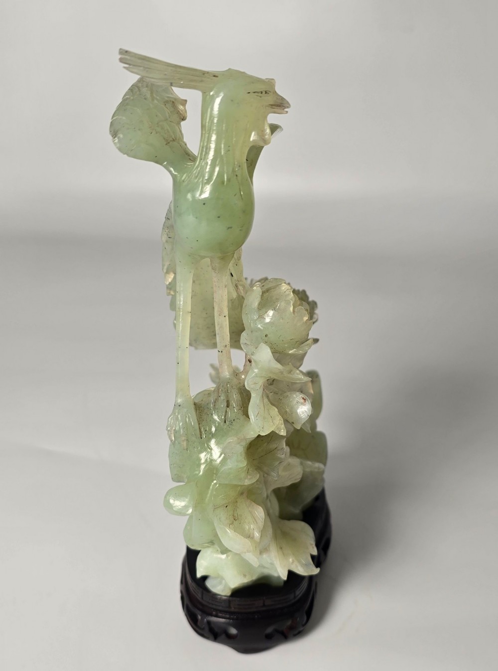 A pale green carved stone sculpture depicting two birds among floral blooms set on a dark carved wood base. View VI