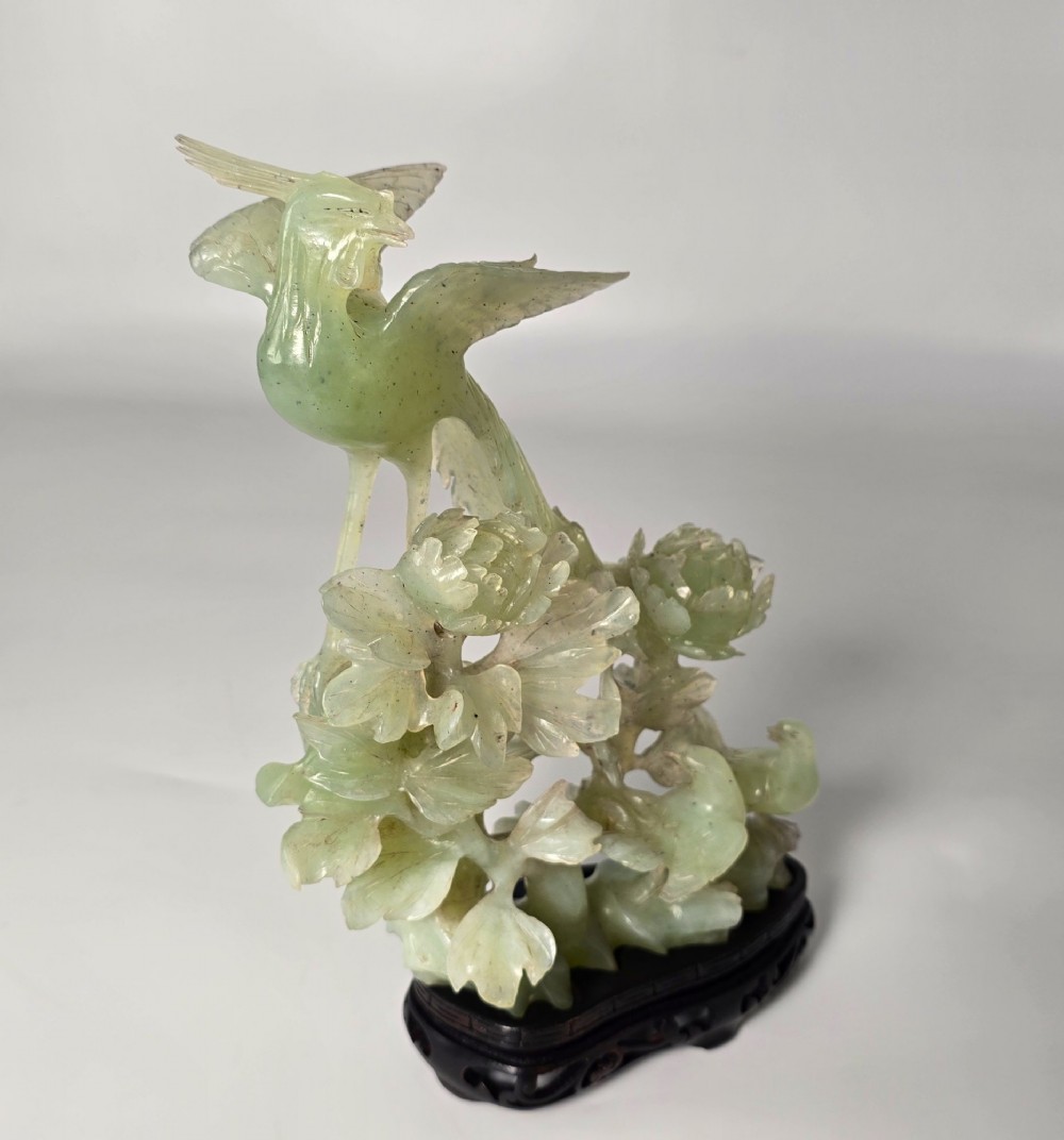 A pale green carved stone sculpture depicting two birds among floral blooms set on a dark carved wood base. View VII