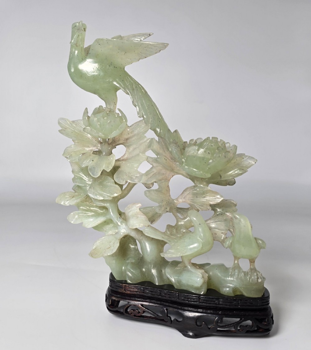 A pale green carved stone sculpture depicting two birds among floral blooms set on a dark carved wood base. View VIII