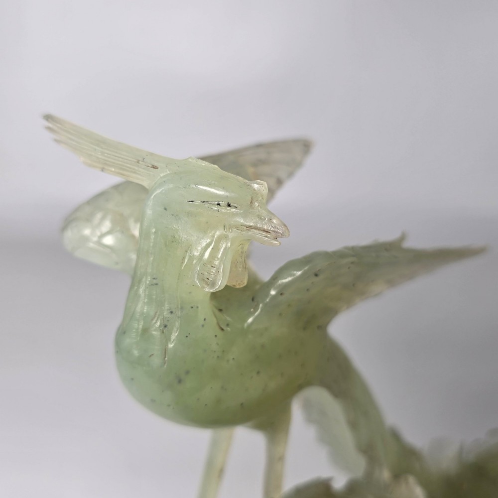 A pale green carved stone sculpture depicting two birds among floral blooms set on a dark carved wood base. View IX