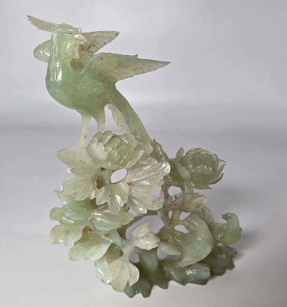 A pale green carved stone sculpture depicting two birds among floral blooms set on a dark carved wood base. View XI