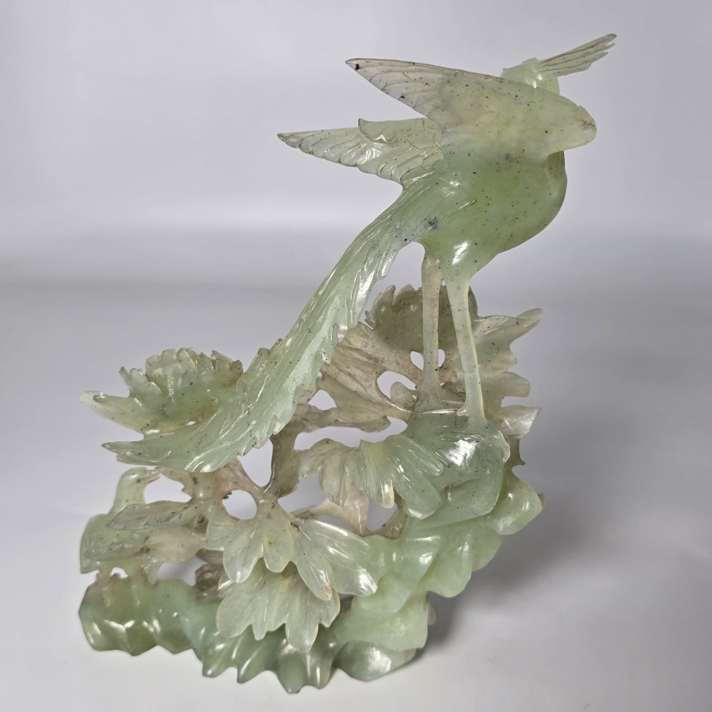 A pale green carved stone sculpture depicting two birds among floral blooms set on a dark carved wood base. View XII