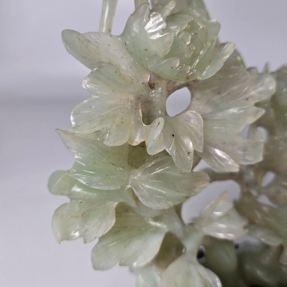A pale green carved stone sculpture depicting two birds among floral blooms set on a dark carved wood base. View XIV
