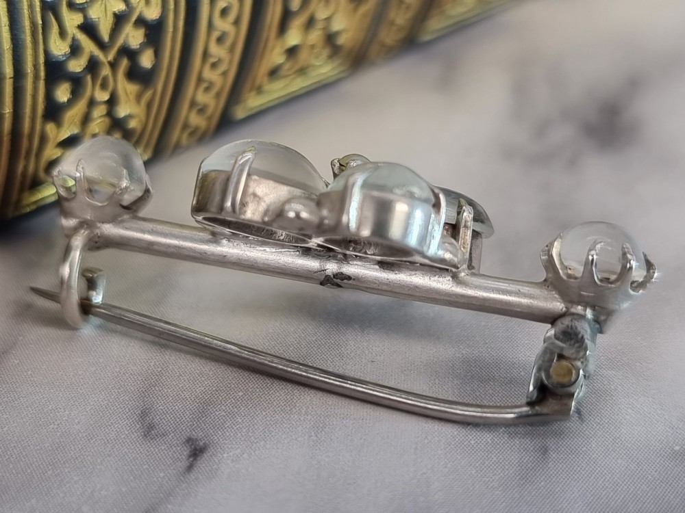 An antique silver bar brooch featuring a central flower cluster of oval cabochon moonstones flanked by single moonstones on either side. View II