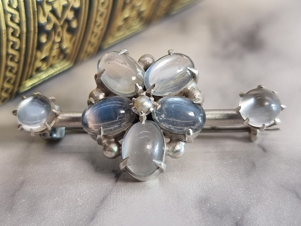 An antique silver bar brooch featuring a central flower cluster of oval cabochon moonstones flanked by single moonstones on either side. View IV